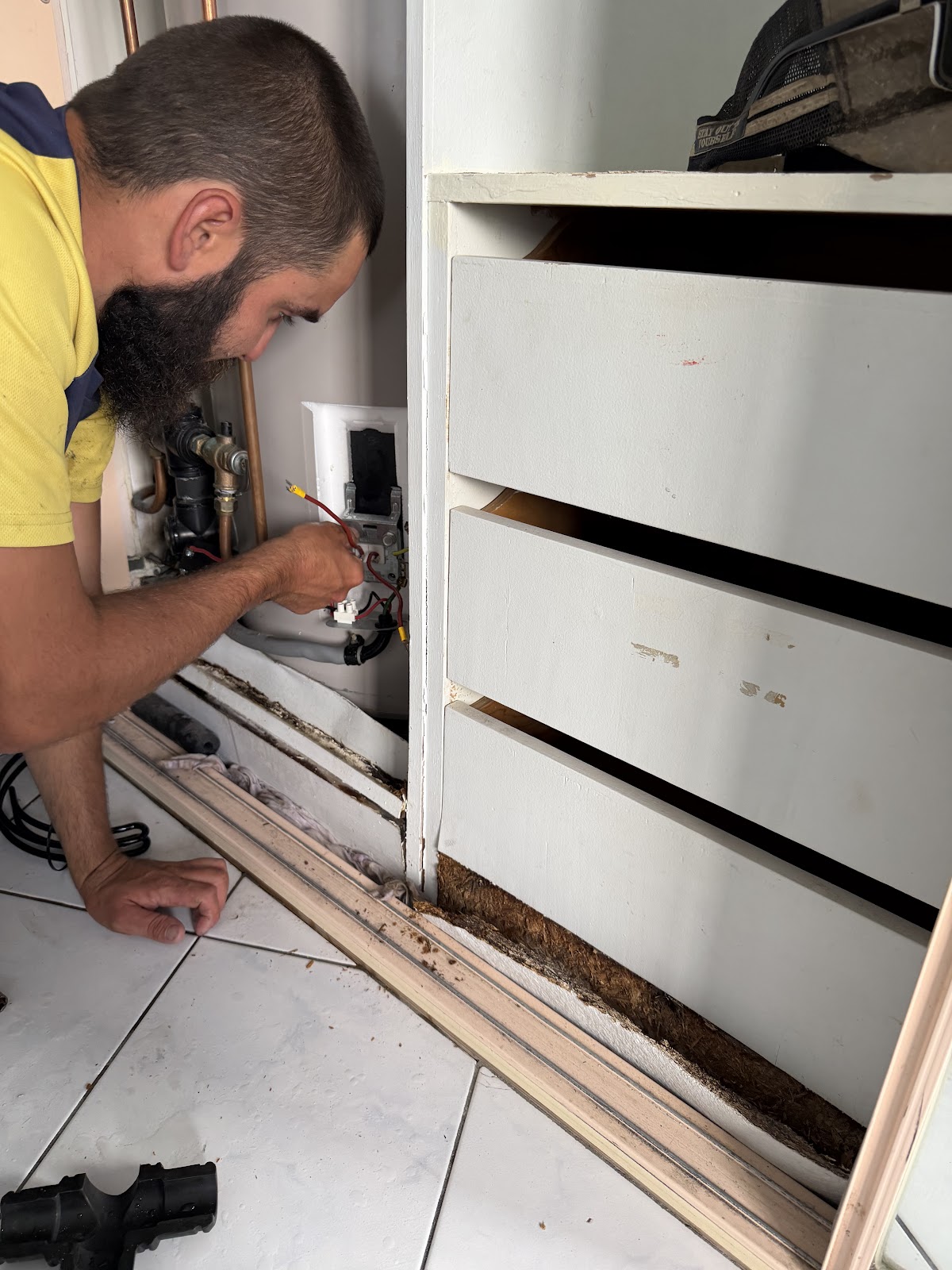 A K&K plumber in hi vis working on pipes behind kitchen cabinetry